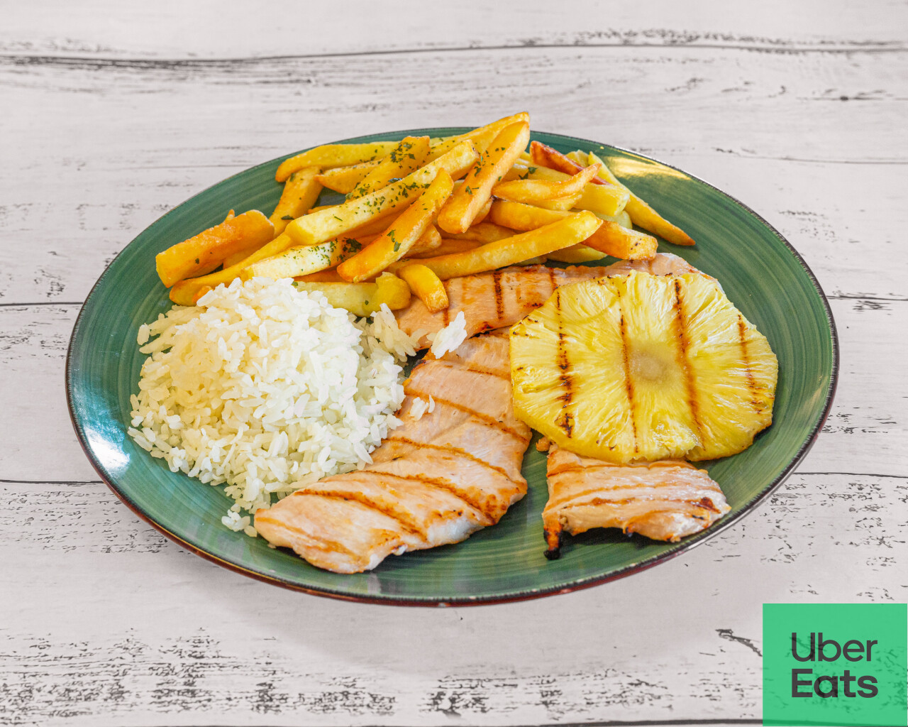 Close-up of a meal plate featuring chicken, rice, fries, lettuce, and tomato on a woven mat.