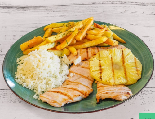Close-up of a meal plate featuring chicken, rice, fries, lettuce, and tomato on a woven mat.