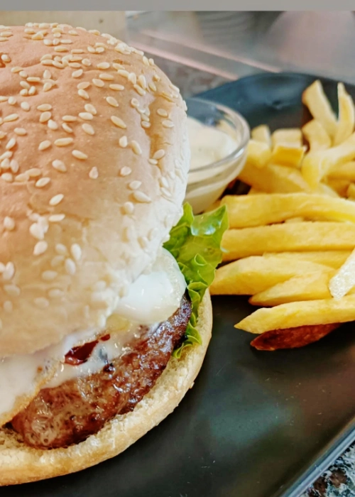 A mouthwatering gourmet burger with lettuce, tomato, cheese, and sesame bun on a wooden board.